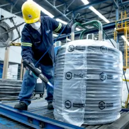 Worker wrapping a coil of steel wire with plastic wrap